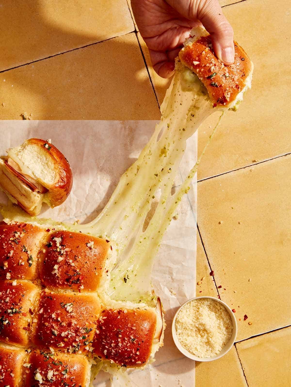A hand grabbing a slider from a piece parchment with a big cheese pull.