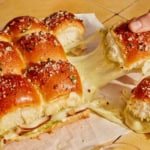 Hawaiian roll sliders with a hand pulling one apart.