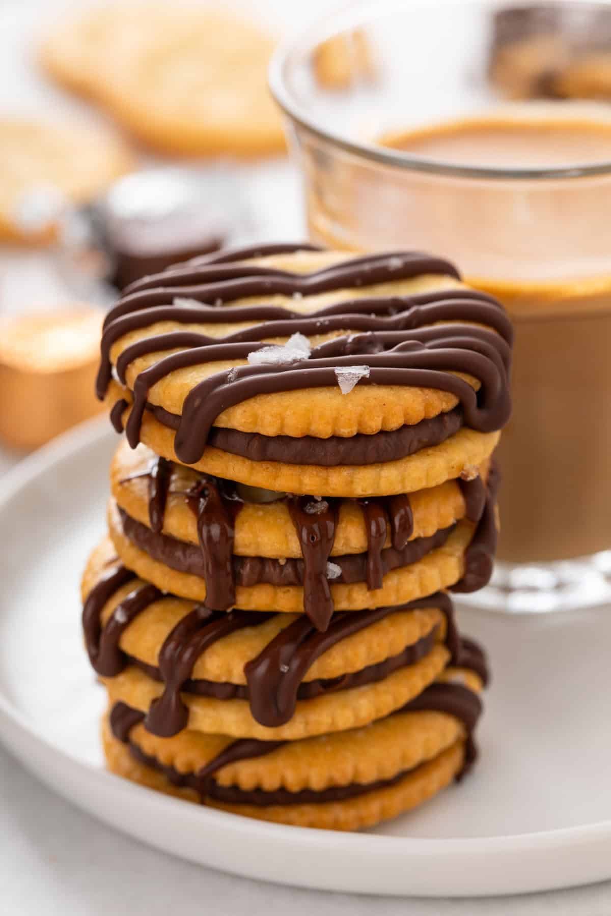 Stack of rolo ritz cracker cookies next to an iced coffee on a white plate.