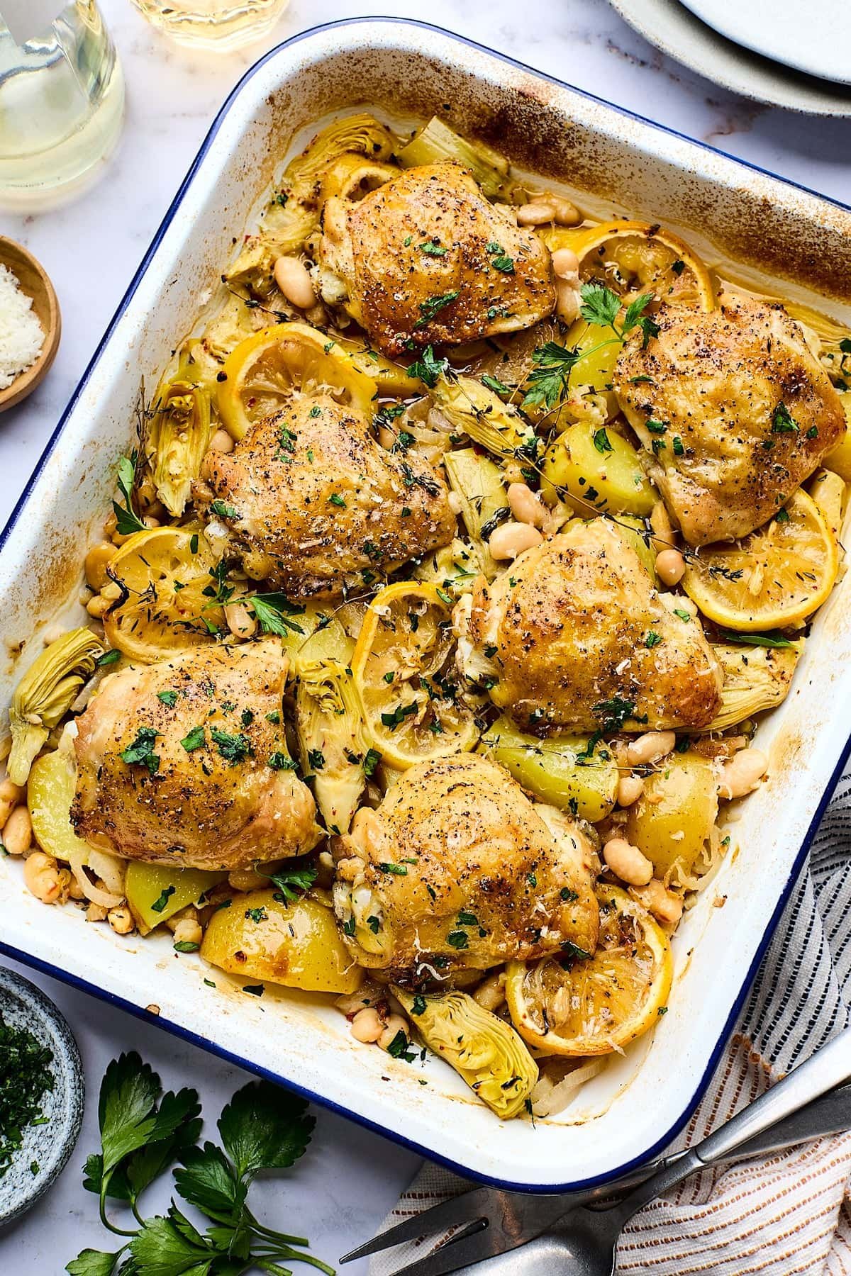 Oven-Roasted Chicken with Potatoes and White Beans in white baking dish with herbs.