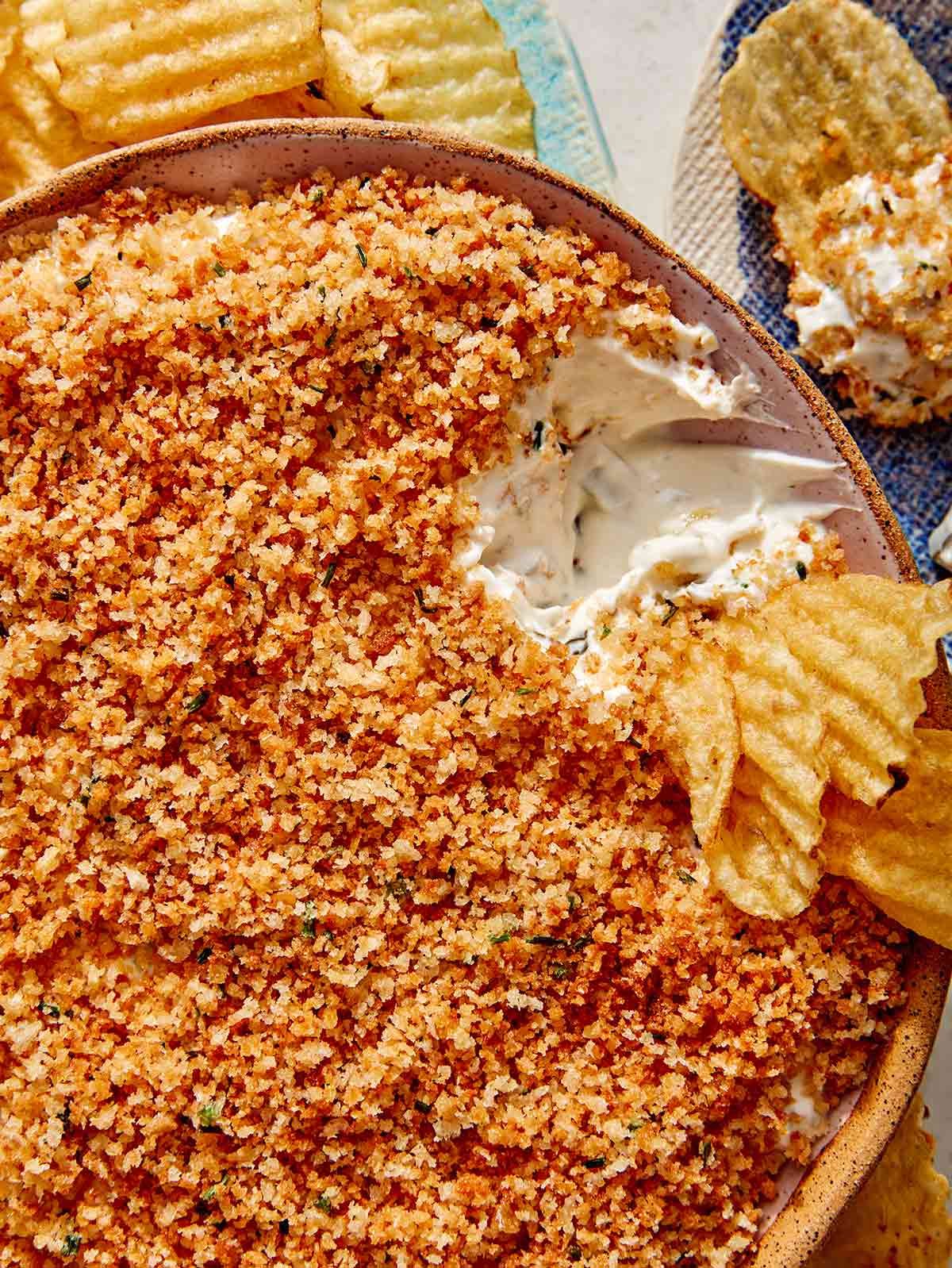 Fried pickle dip with potato chips being dipped in it.