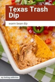 Tortilla chip in a pan of texas trash dip. Text overlay includes recipe name.