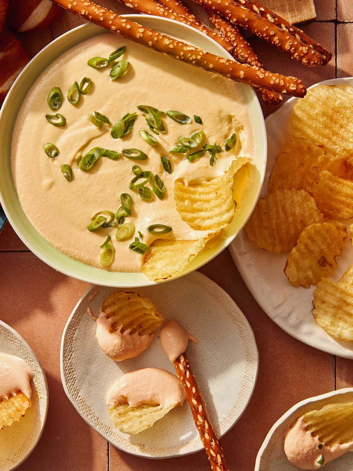 Chips being dipped in a bowl of beer cheese with plates of dipped pretzels on the side.