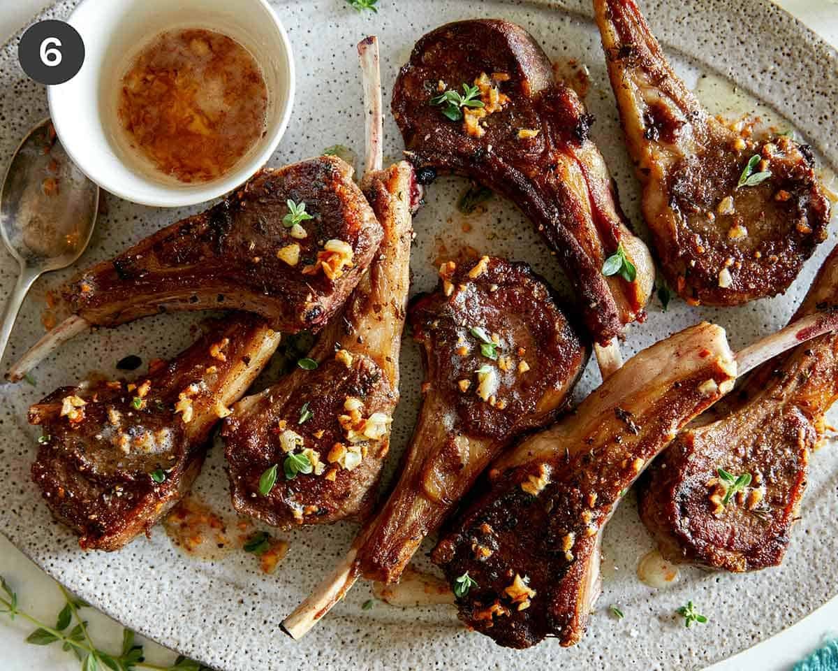 Garlic butter lamb chops recipe on a platter with plates next to it.