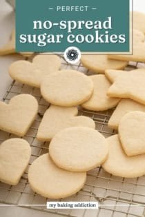 Assorted shapes of no-spread sugar cookies arranged on a wire rack on a countertop. Text overlay includes recipe name.
