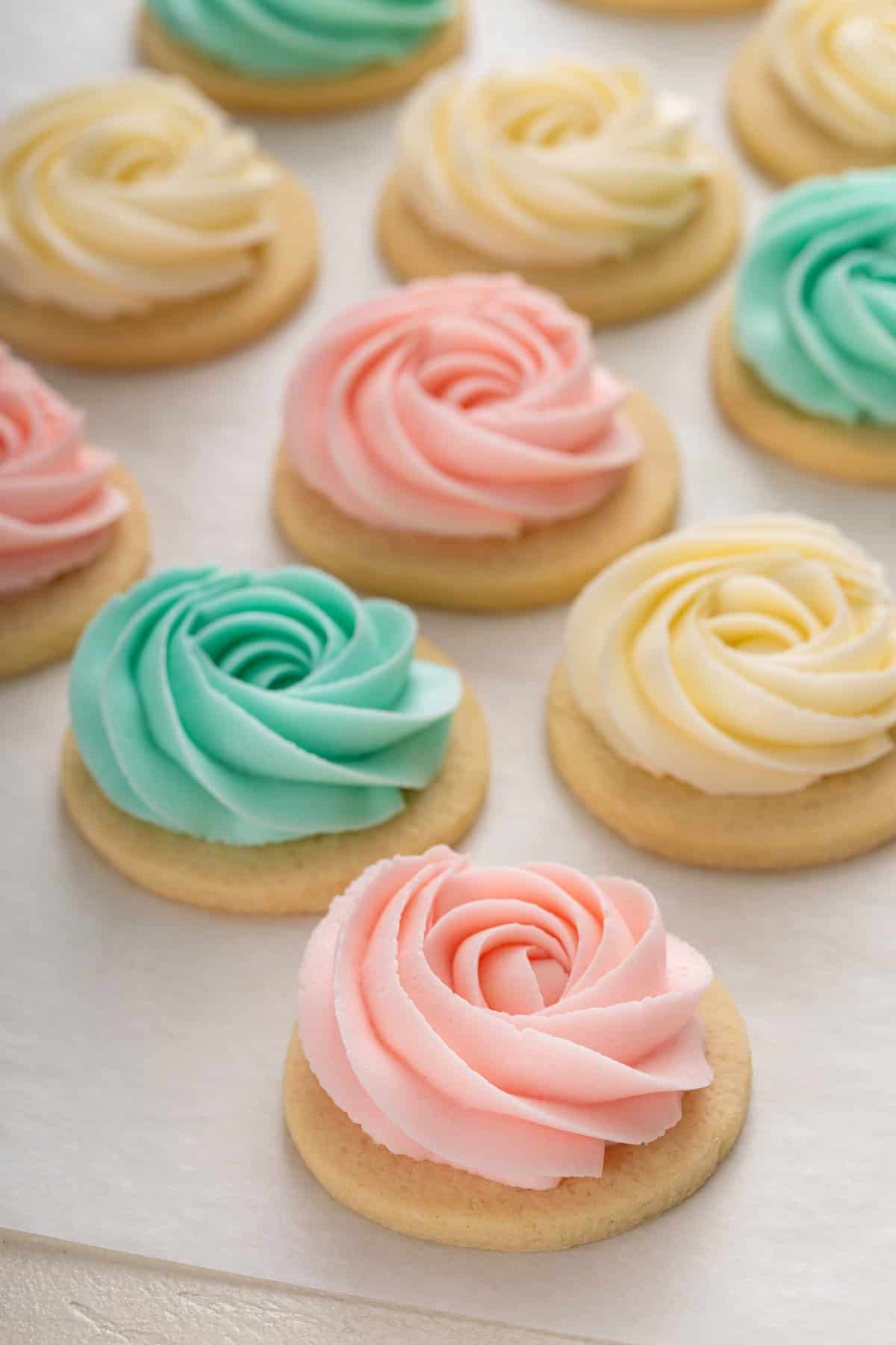 Sugar cookie frosting piped into rosettes in three different colors on round sugar cookies.