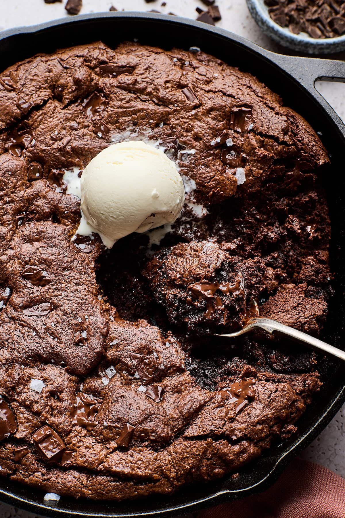 close up of double chocolate skillet cookie with scoop of vanilla ice cream and spoon. 
