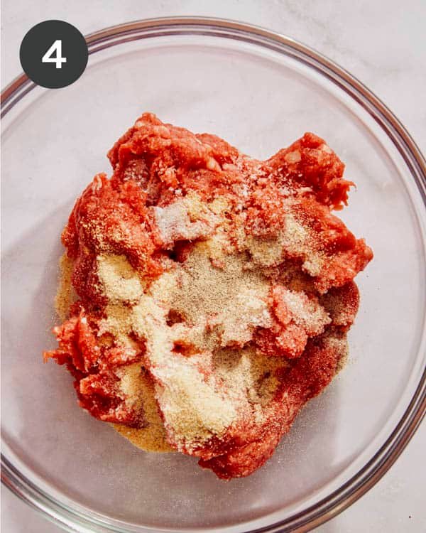 Hamburger meat with spices poured on top in a glass bowl.