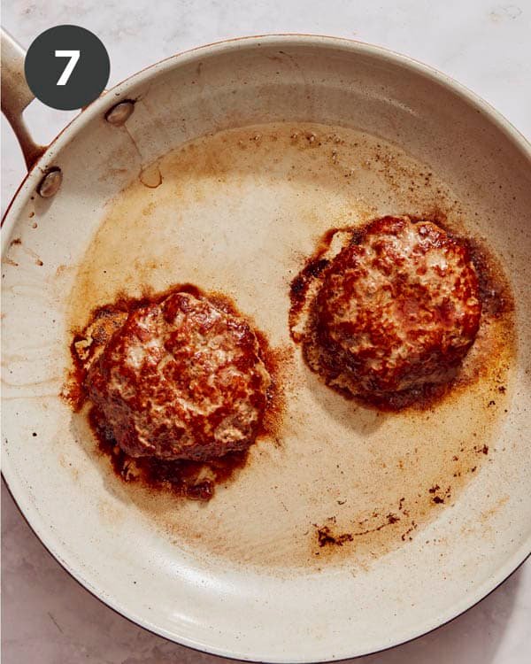 Hamburger patties being cooked in a skillet with oil.