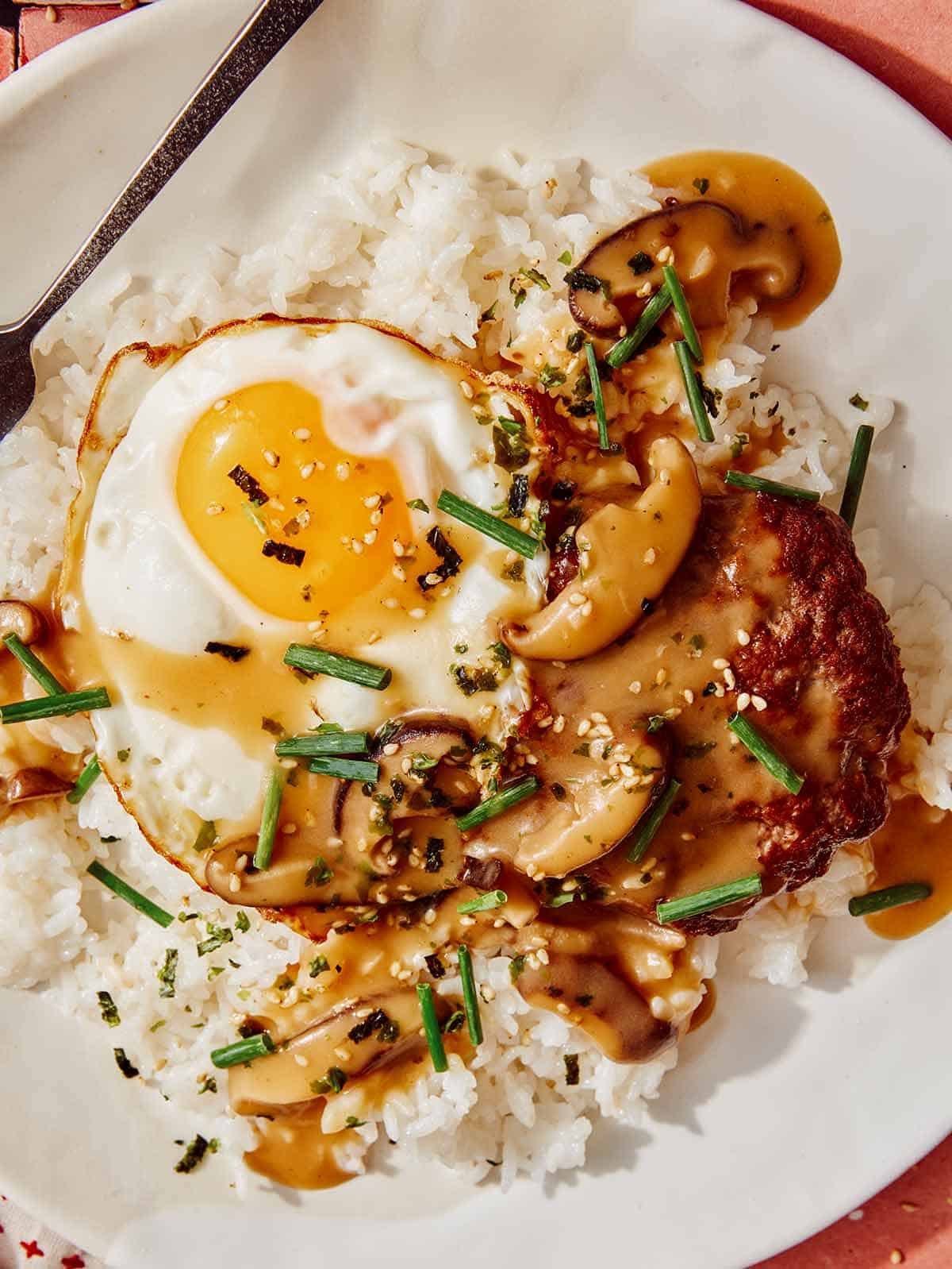 Loco moco up close on a plate with a fork next to it.
