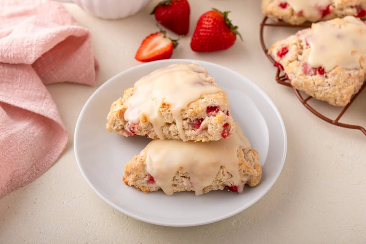 Two strawberry scones arranged on a white plate, with fresh berries in the background.