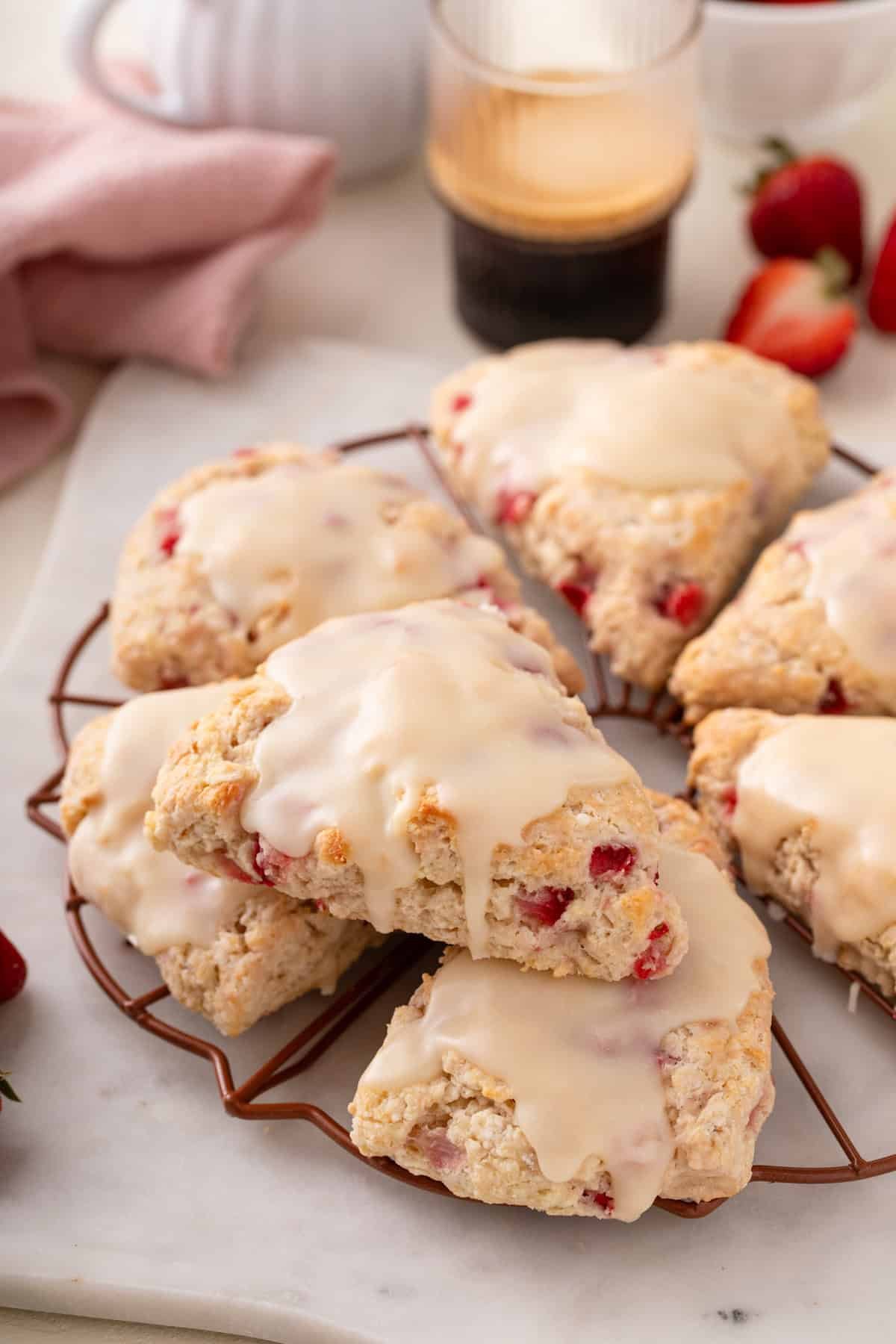 Strawberry scones stacked on a wire rack. A cup of coffee is seen in the background.