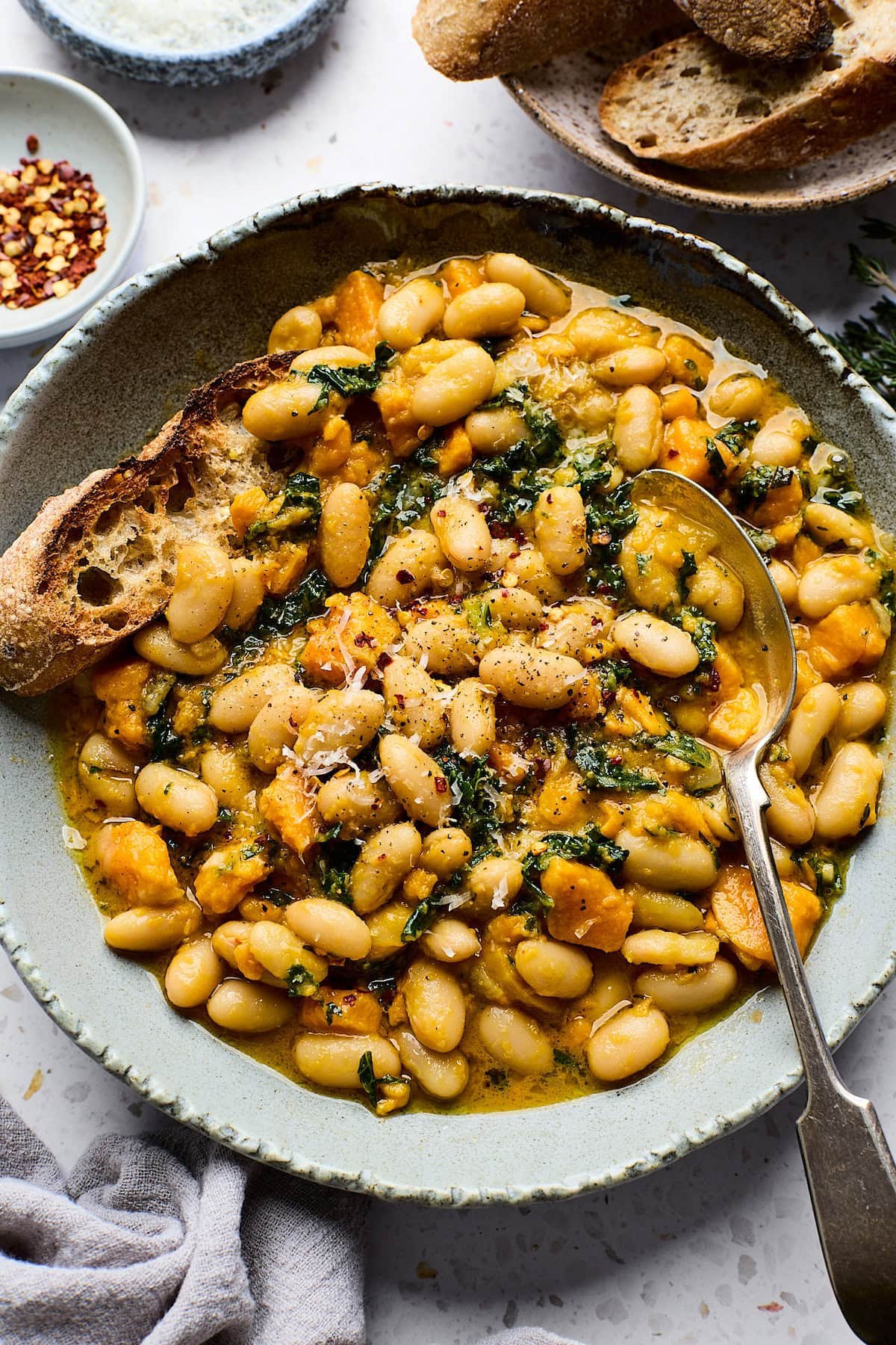 sweet potato and white beans in bowl with spoon and crusty bread. 