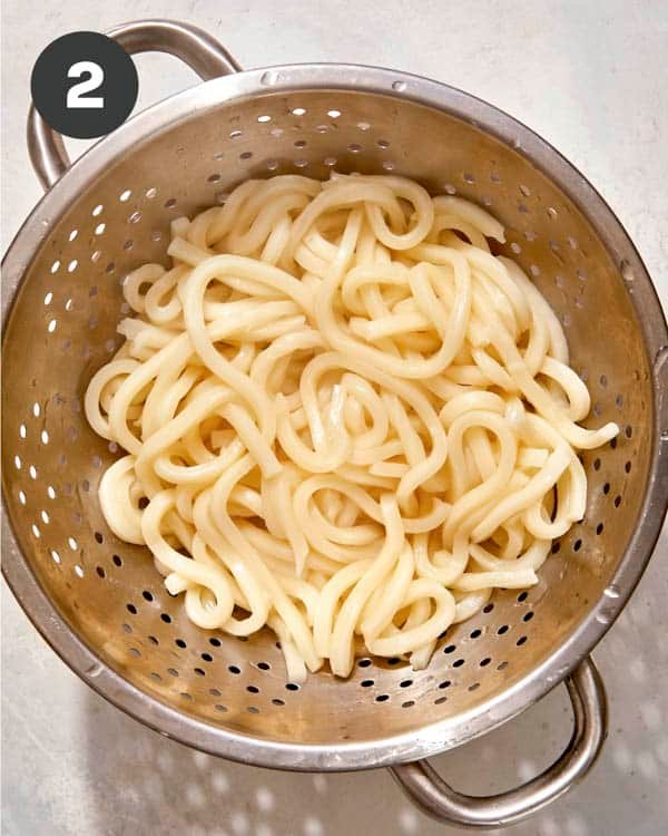 Udon noodles cooked and draining in a colander. 