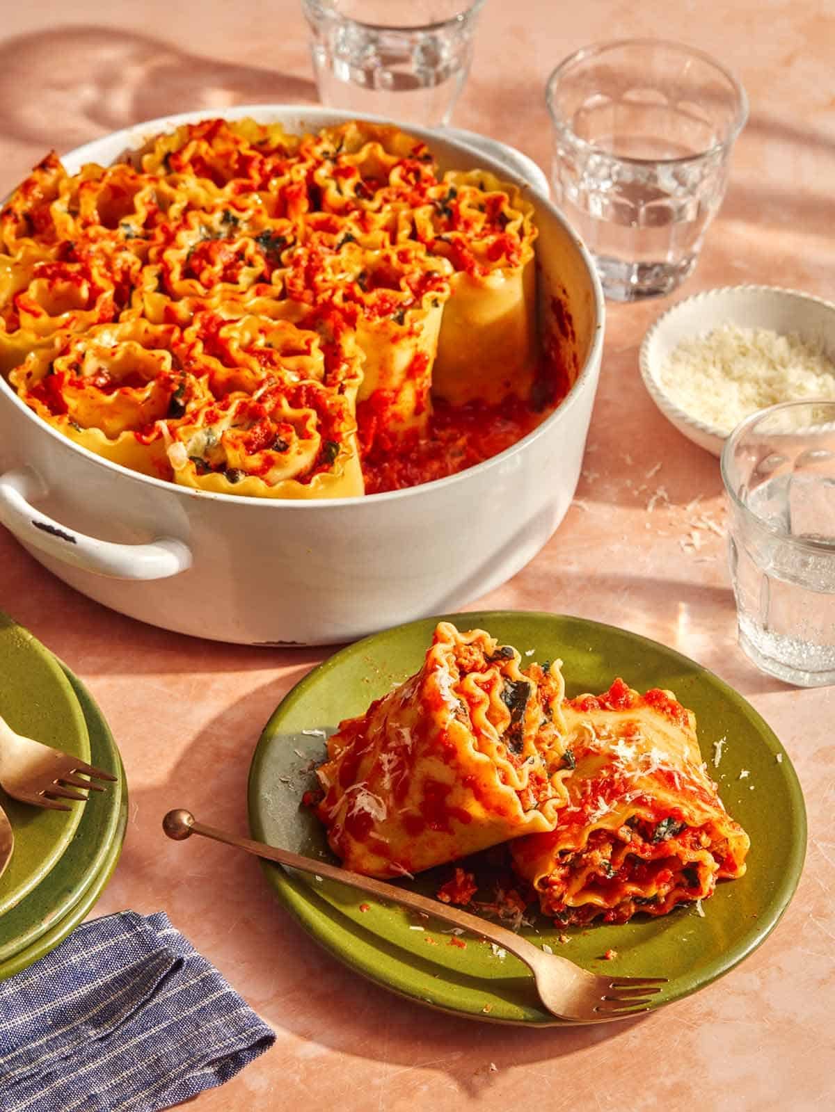 A plate with a serving of two lasagna roll ups and a baking dish with more in the background.
