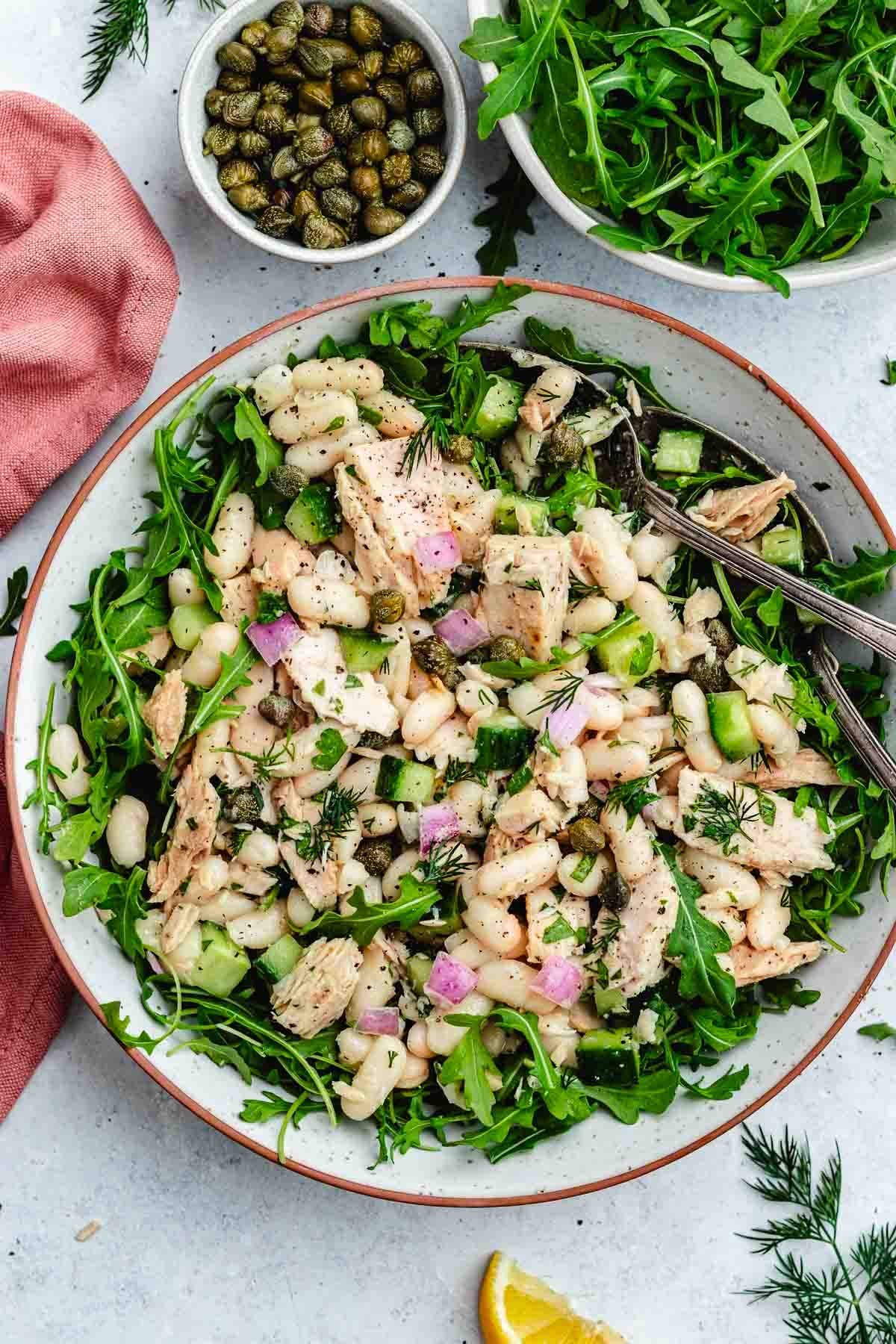 tuna white bean salad over arugula in bowl with serving spoons. 