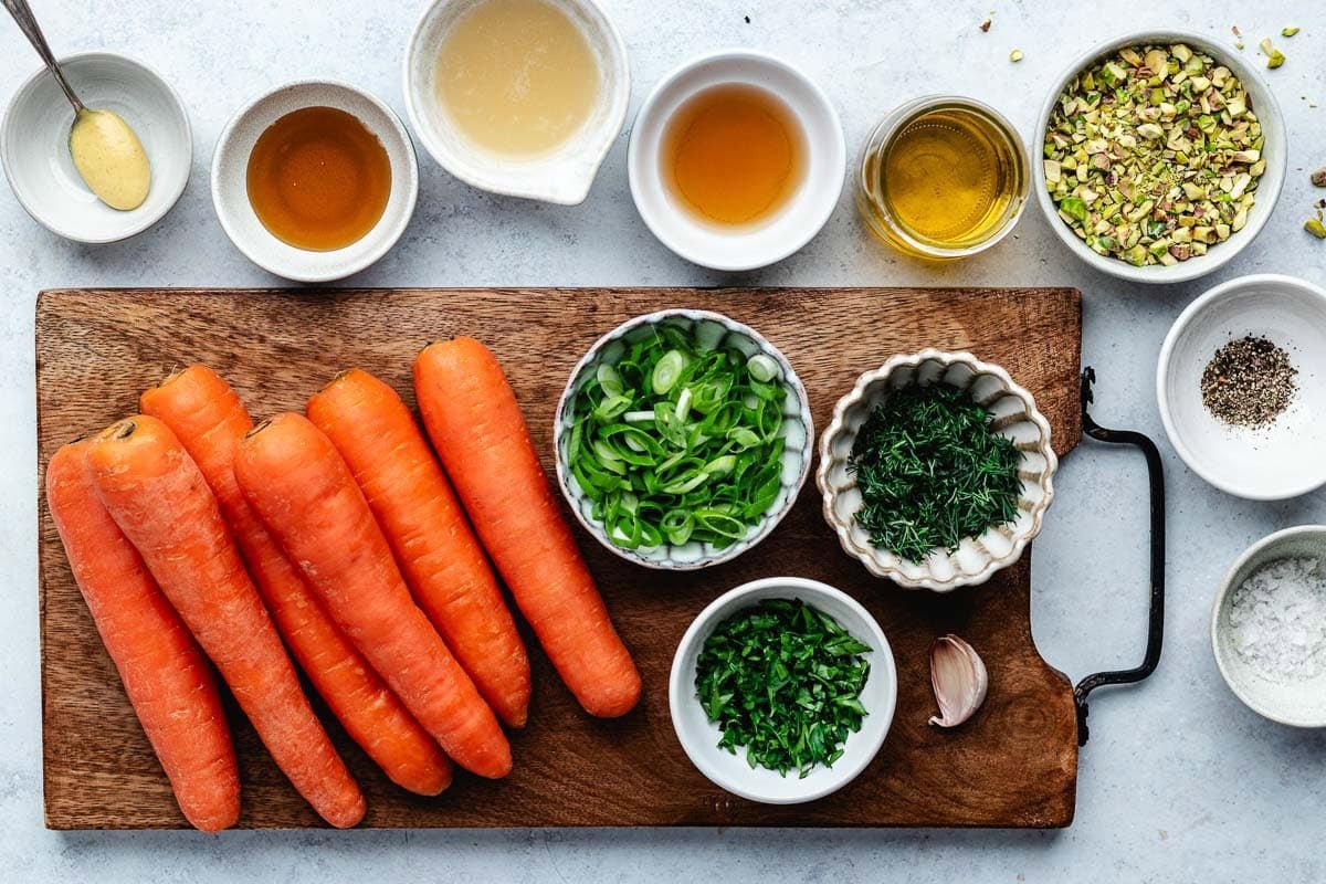 carrots on wood board and ingredients in bowls to make carrot ribbon salad. 