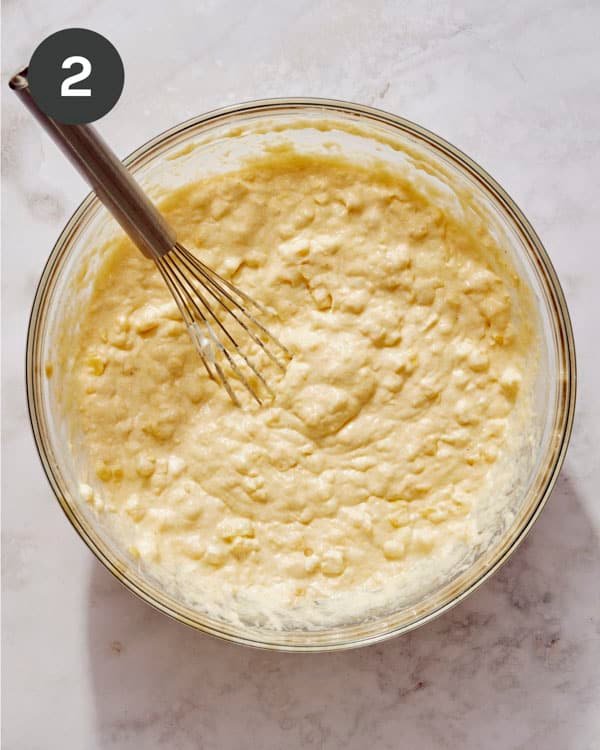 Corn casserole batter being mixed in a glass bowl.