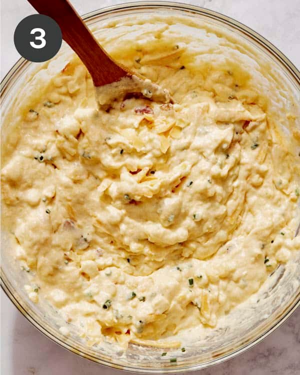 Corn casserole batter mixed together in a glass bowl with some mix ins.