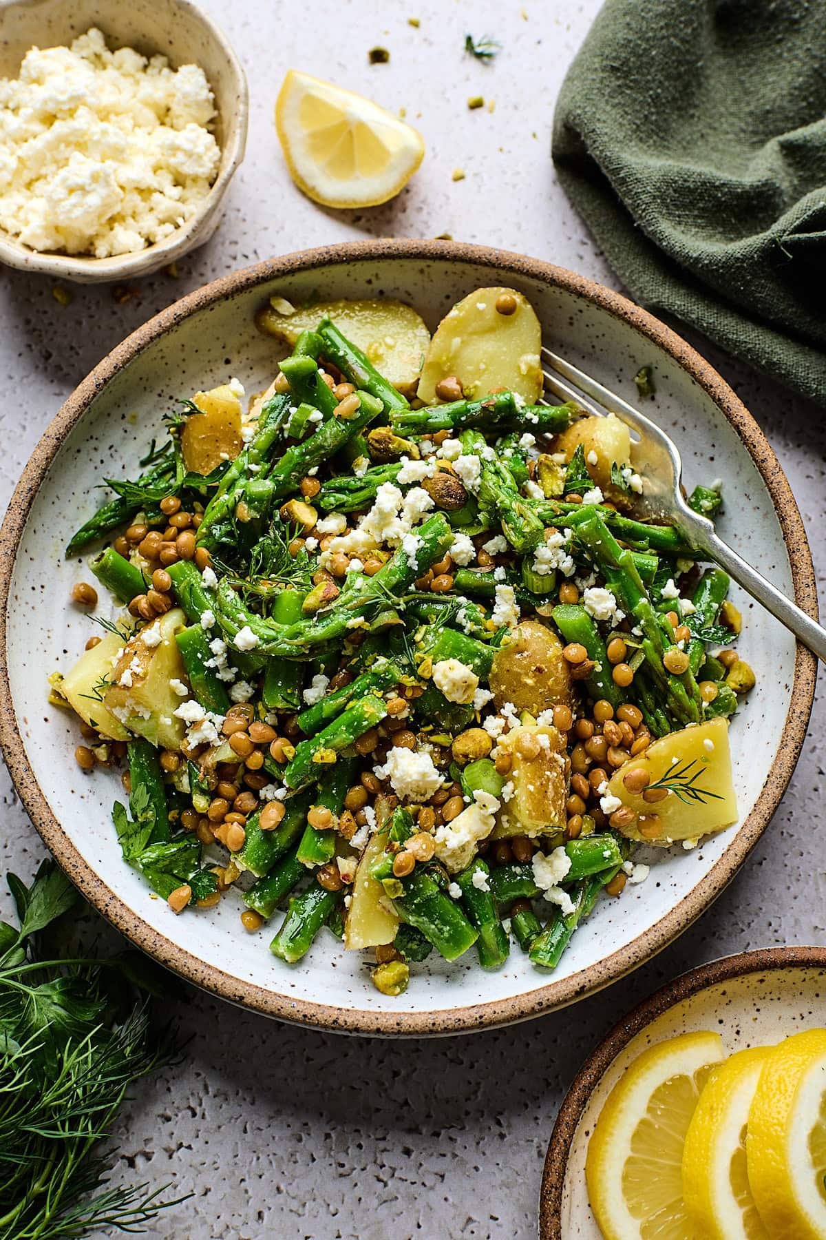 Potato Asparagus Lentil Salad with Lemon Dijon Dressing with feta and herbs on plate with fork. 