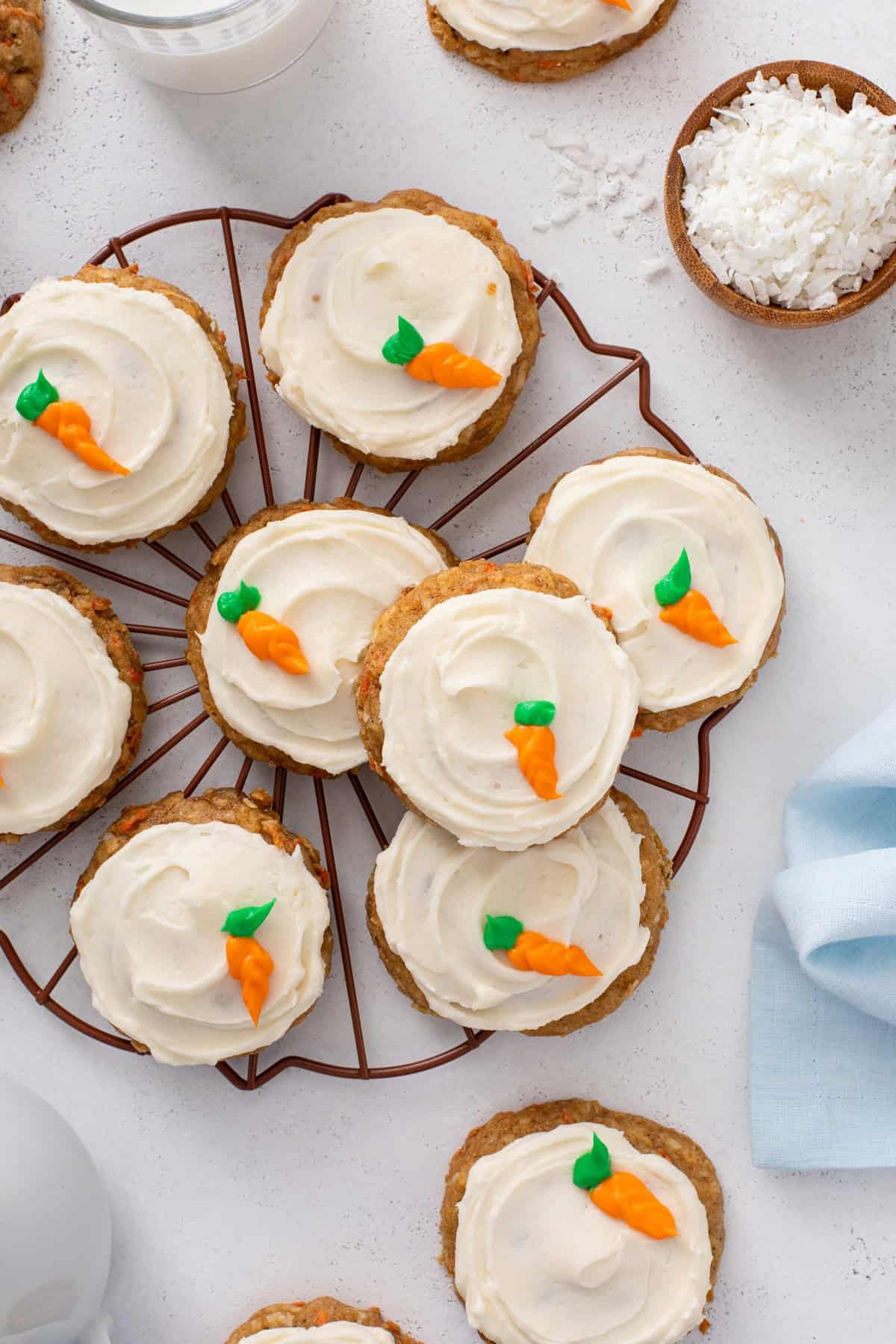 Overhead view of frosted carrot cake cookies decorated with a frosting carrot arranged on a wire rack.