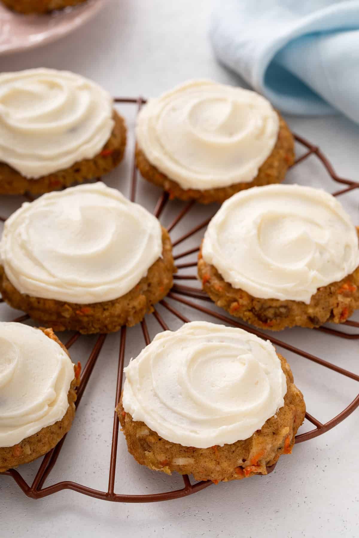 Side view of carrot cake cookies topped with cream cheese frosting on a wire rack.