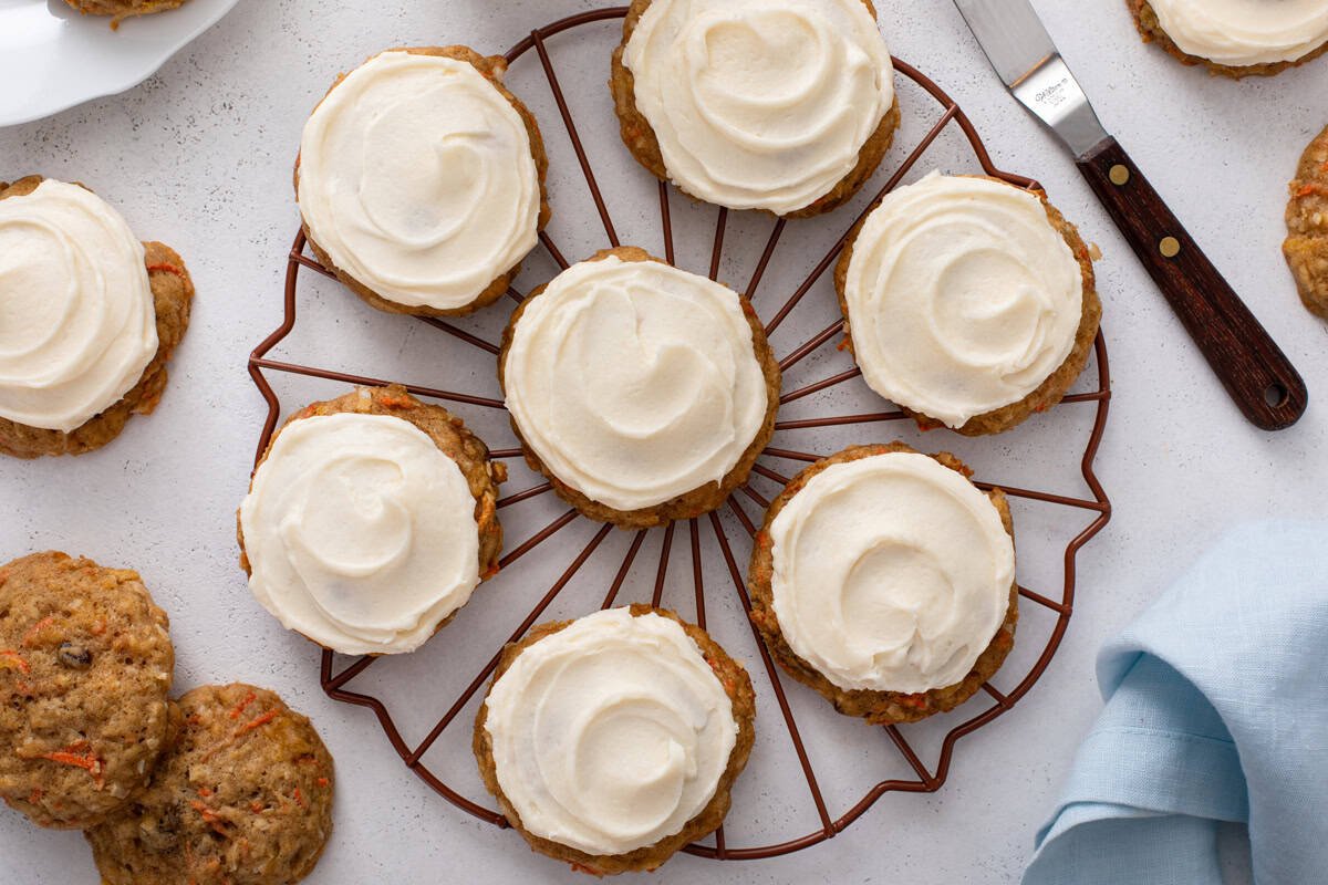Overhead view of carrot cake cookies topped with cream cheese frosting on a round wire rack.