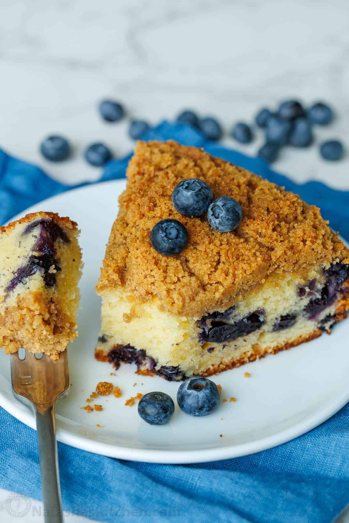 a slice of blueberry coffee cake on a white plate with a bite on a fork