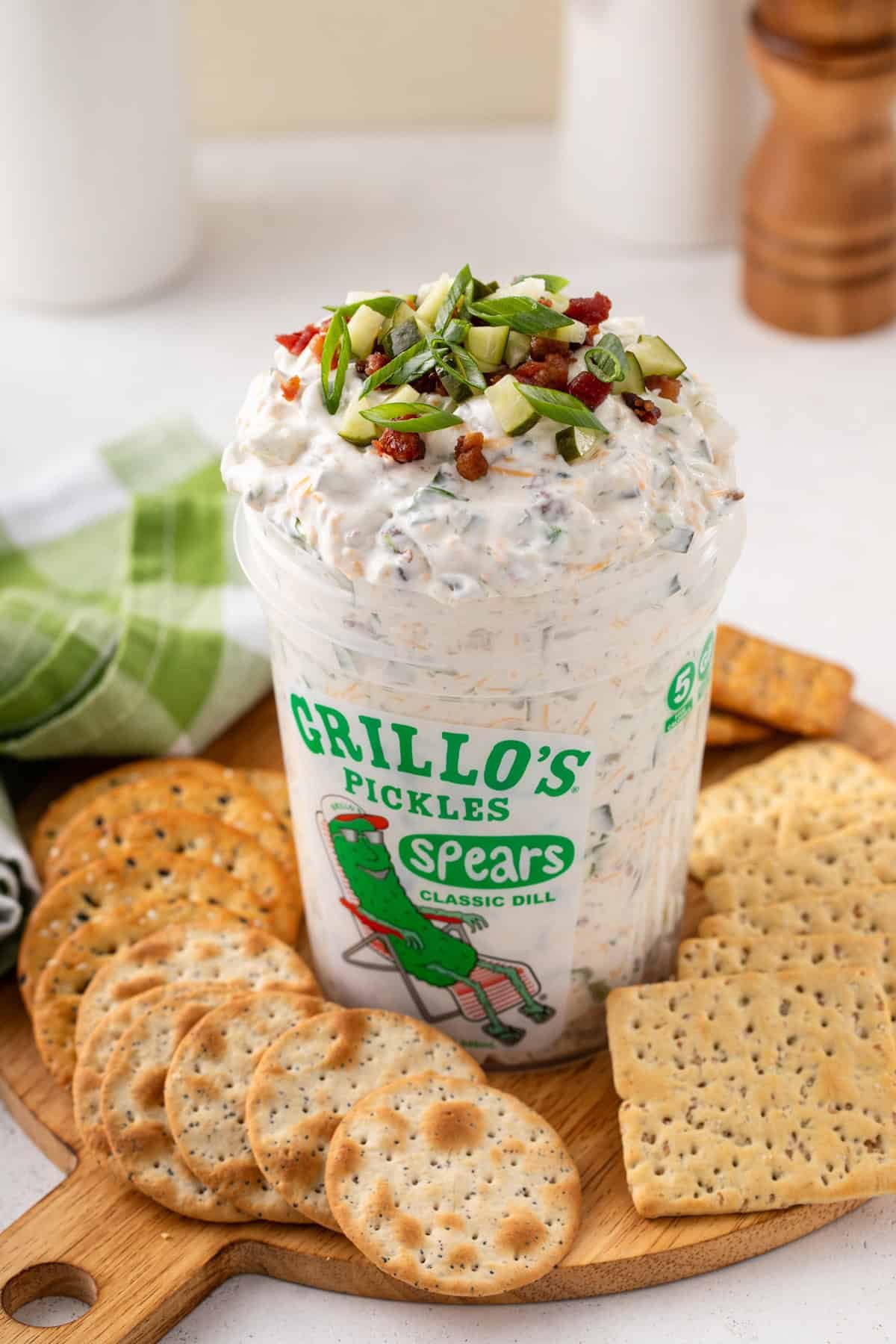 Grillo's pickle dip in a grillo's pickle container on a board surrounded by crackers.