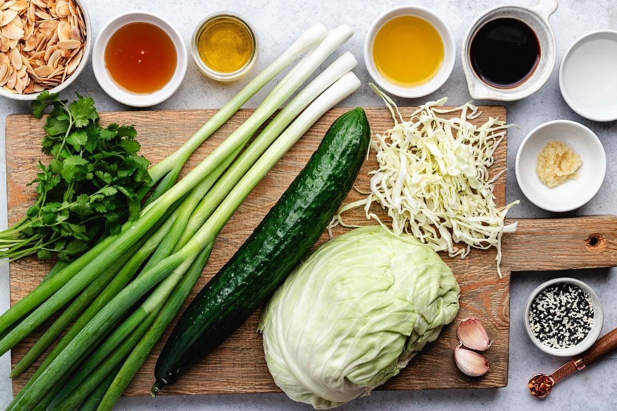 ingredients on wood board and in bowls to make sesame cabbage salad. 