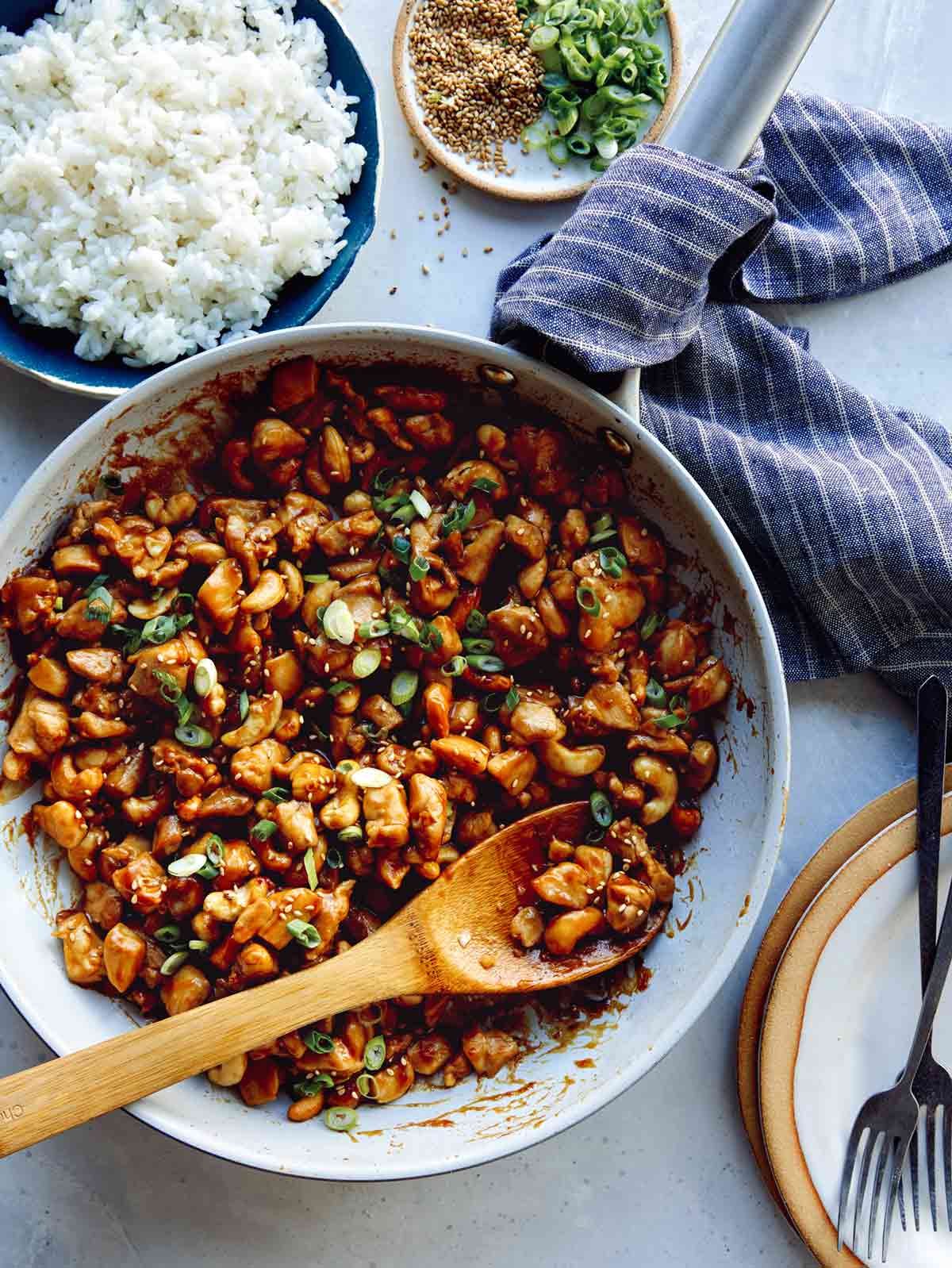Cashew chicken recipe in a skillet with plates and forks on the side.