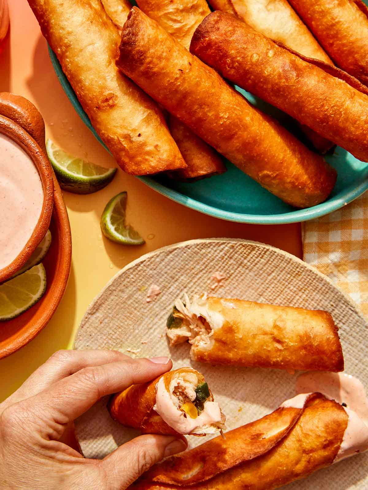 Flautas being served with a hand holding half of one over a plate.