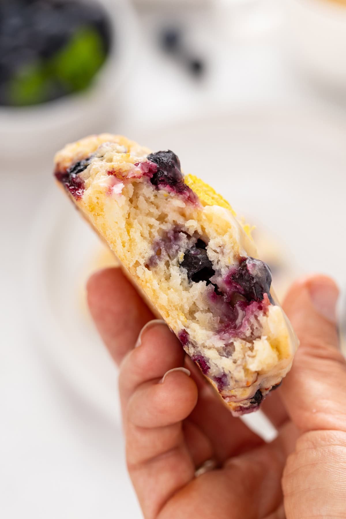 Hand holding up a halved lemon blueberry scone to show the tender crumb.