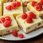Easy raspberry lemon cheesecake bars on a plate with graham cracker crust and strawberries on top.