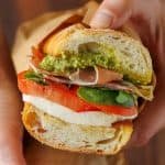 Italian sandwich recipe with layers of mozzarella, deli meat, pesto, and fresh tomato with basil