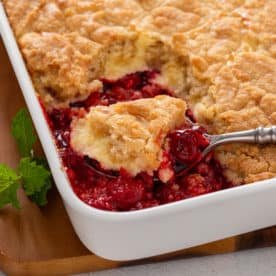 Spoon serving cherry cheesecake cake out of a pan.