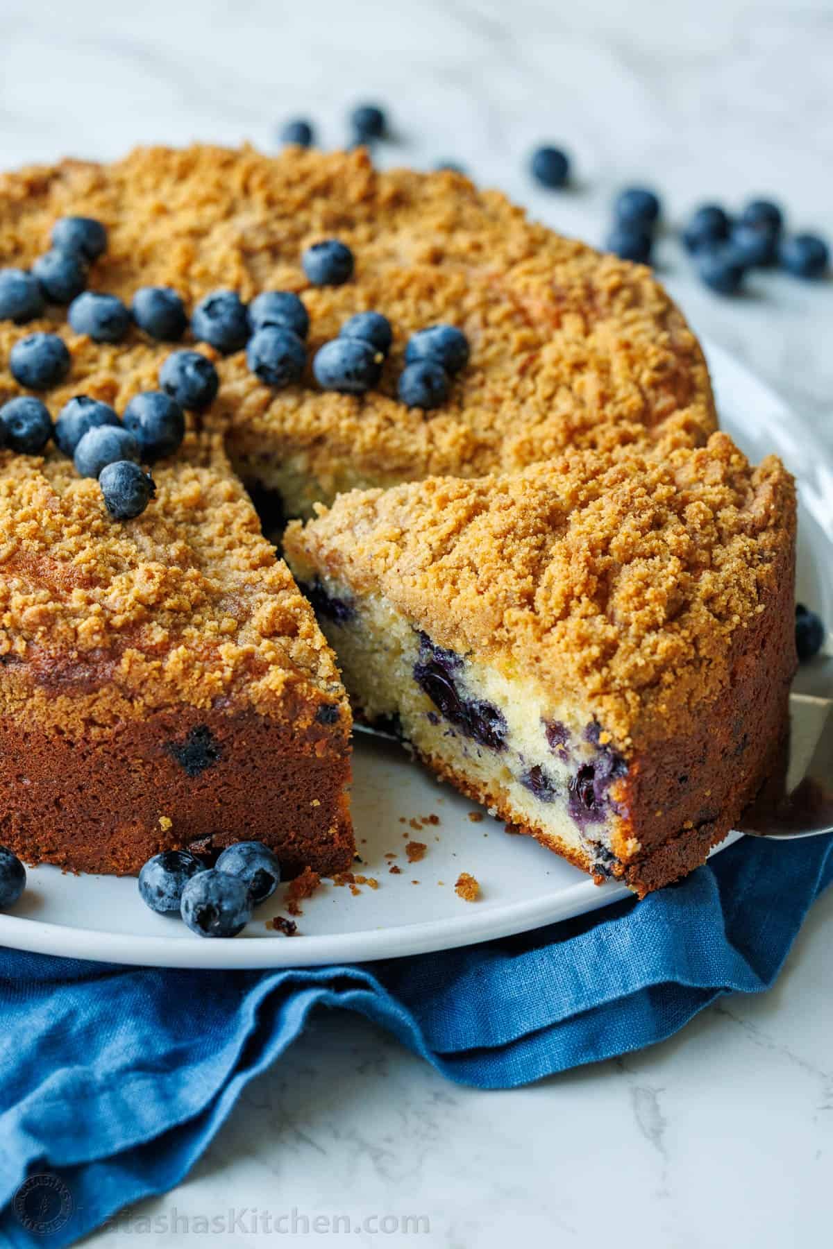 slice cut out of a whole blueberry coffee cake with fresh blueberries on top