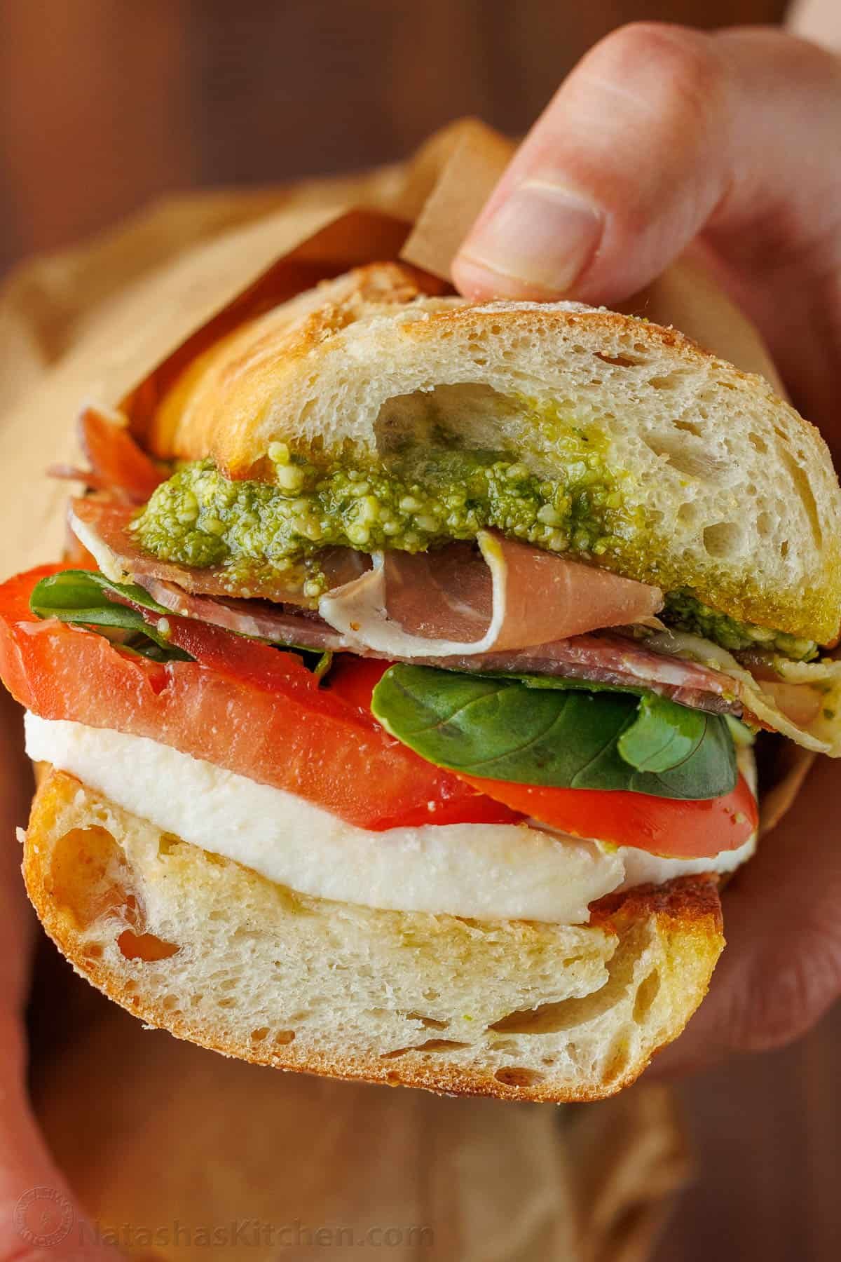 Homemade Italian sub sandwich with a slice of tomato, fresh mozzarella cheese, basil, pesto, meat and toasted bread