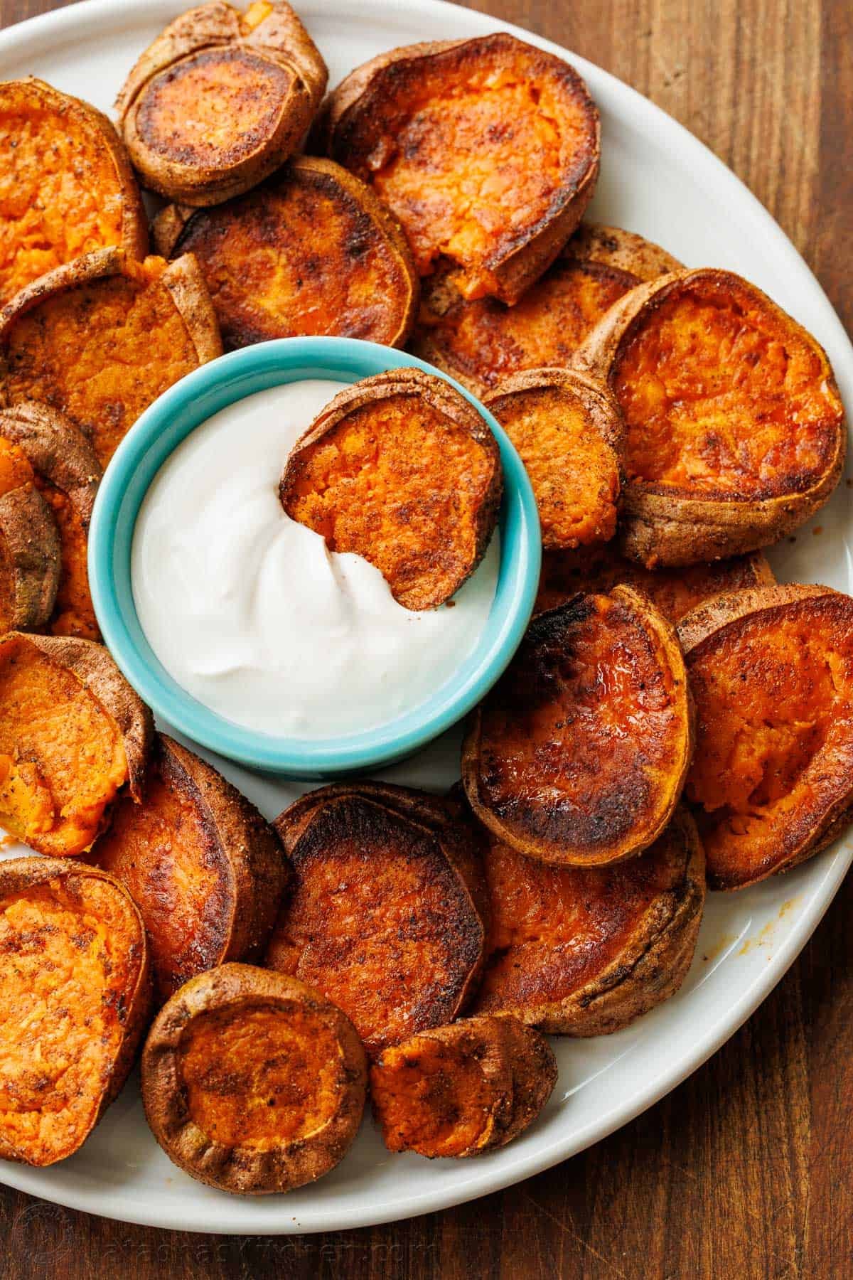 Smashed sweet potatoes with lemon garlic dipping sauce served on a white plate