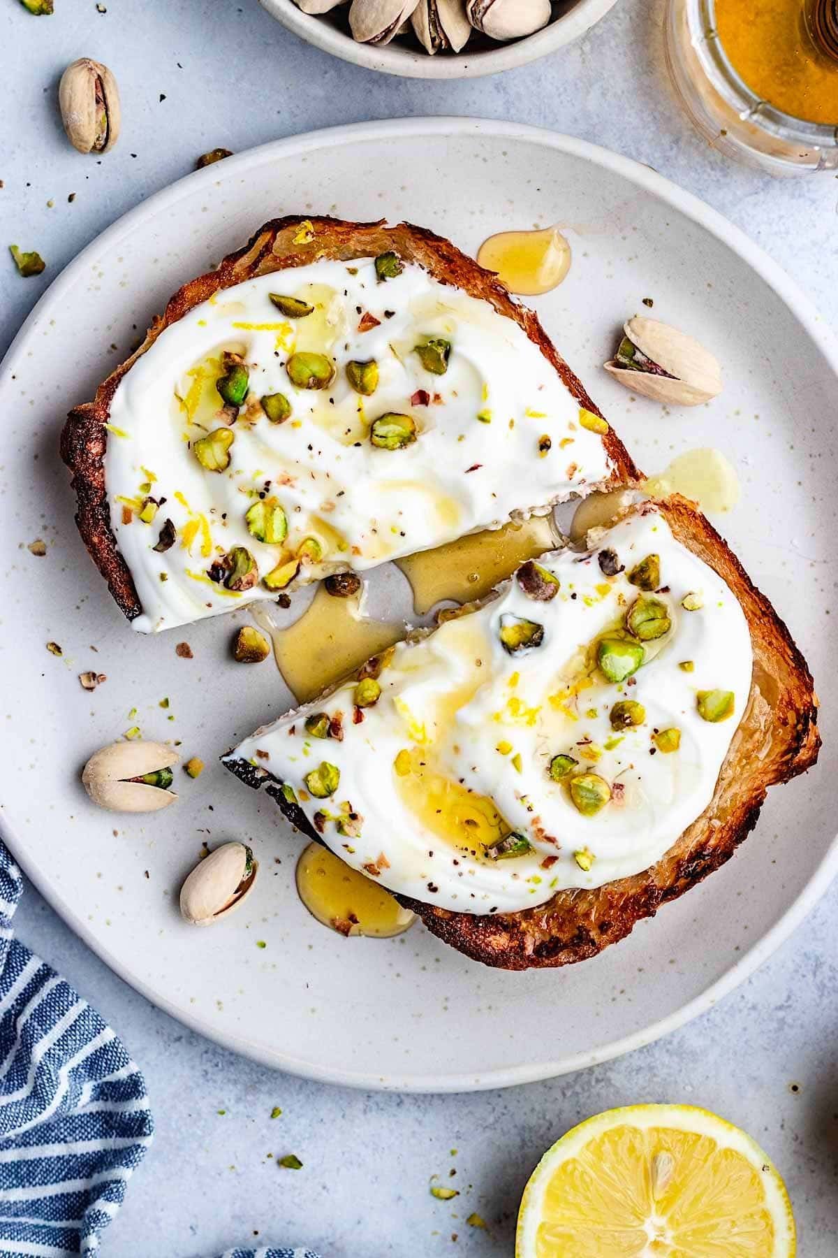 whipped ricotta toast with pistachios and honey on plate. 