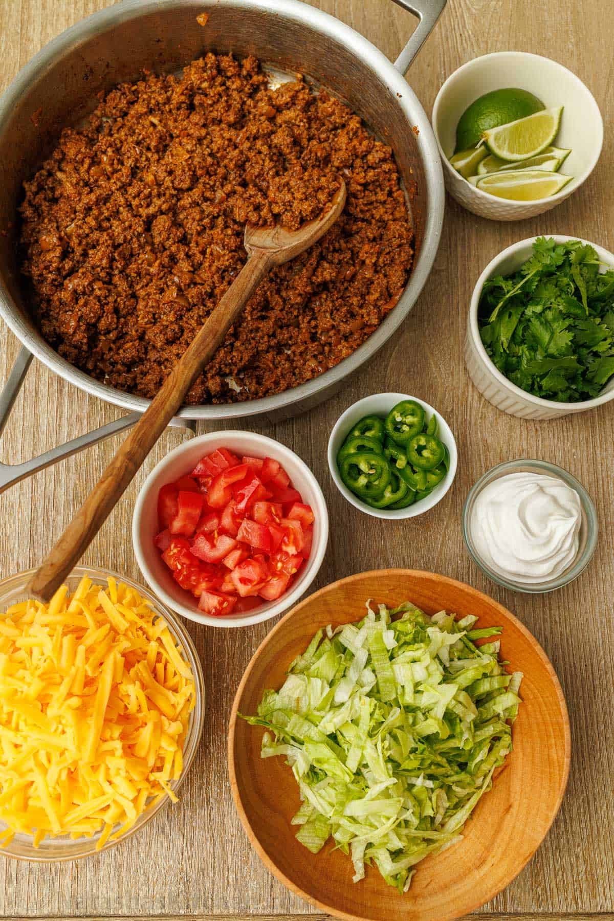 Mexican toppings including cooked meat, lime slices, cilantro, sliced jalapeños, sour cream, chopped tomatoes, shredded cheese and lettuce