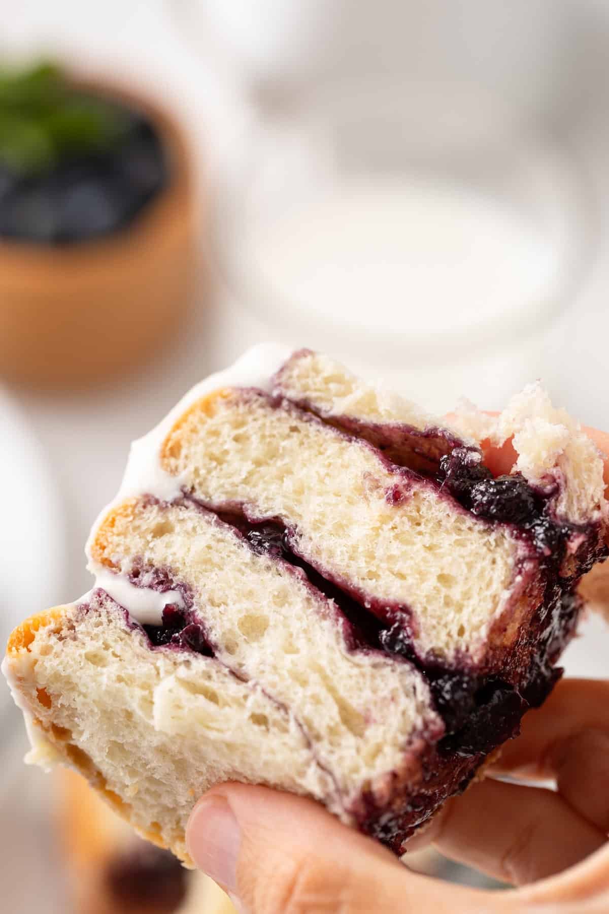 Hand holding up half of a blueberry sweet roll to the camera.