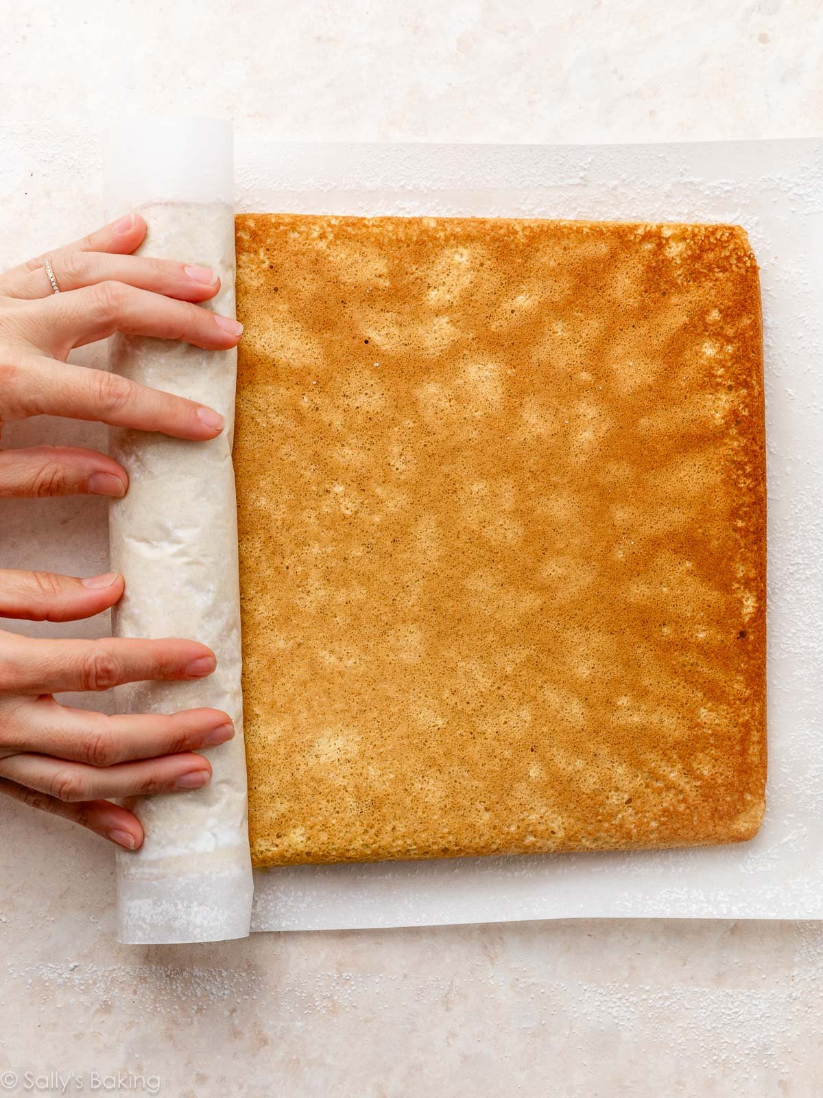 hands rolling up cake roll in parchment paper.