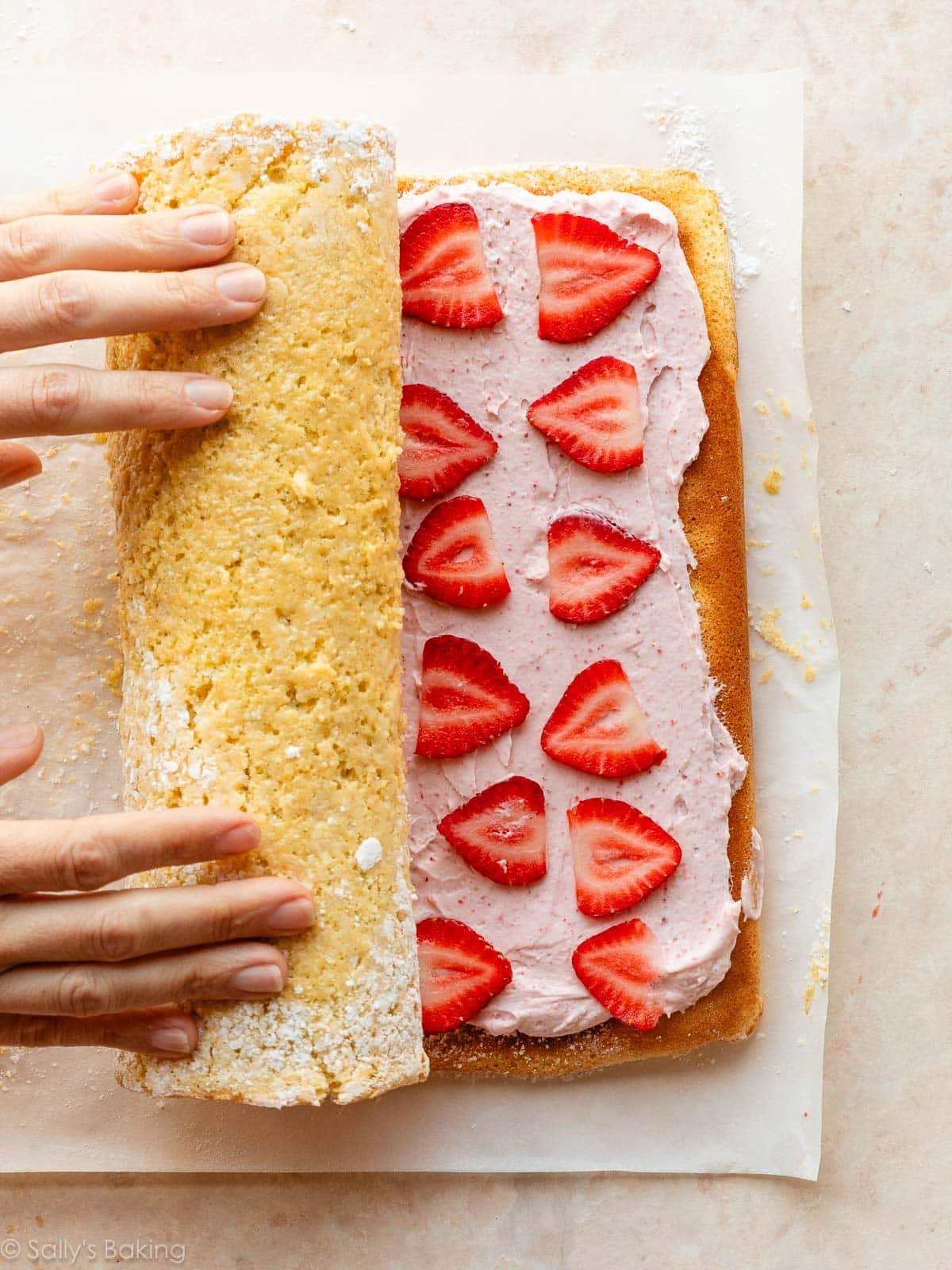 hands rolling up strawberry-lined cake roll.