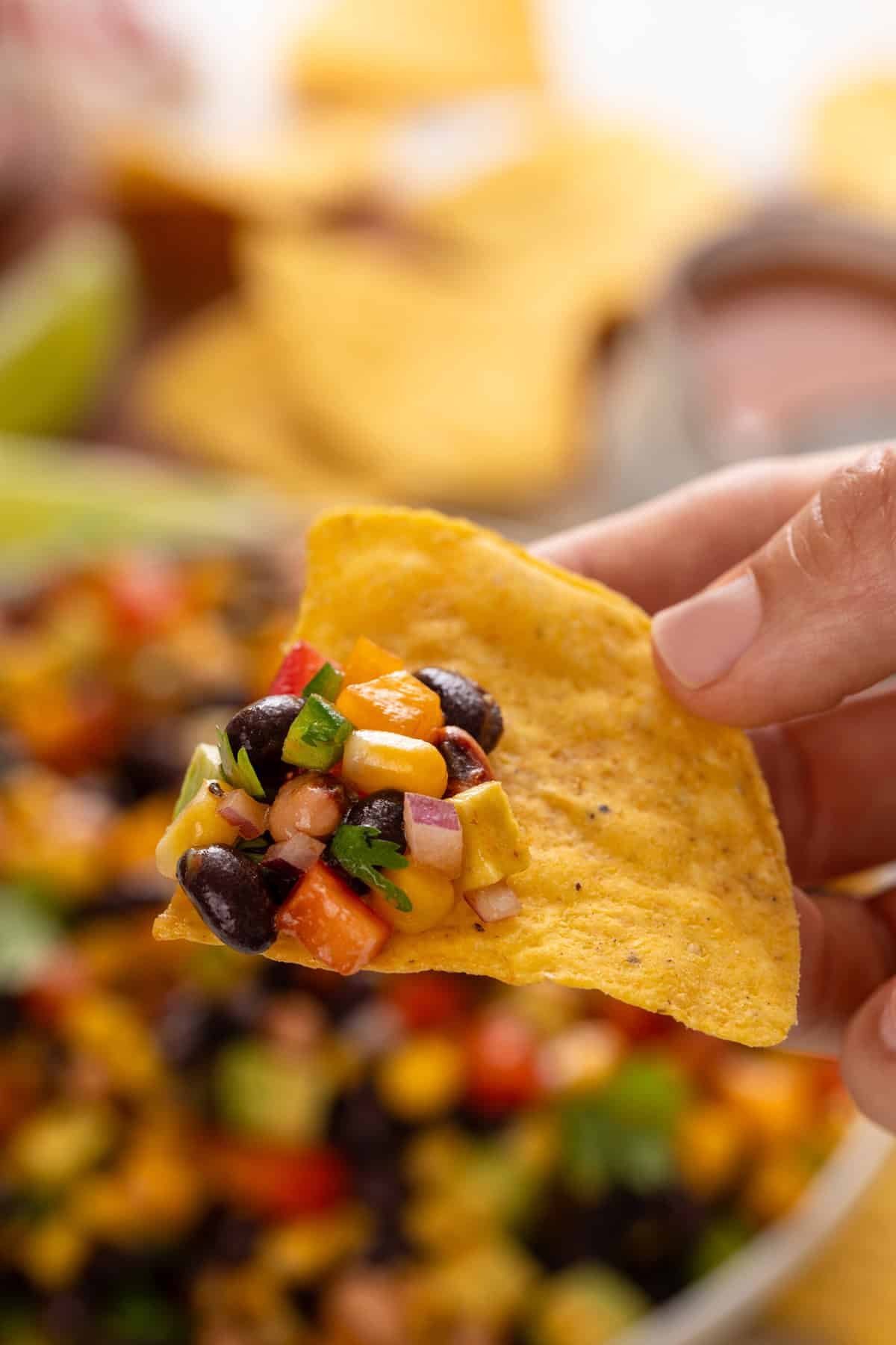 Hand holding up a tortilla chip with cowboy caviar on it.