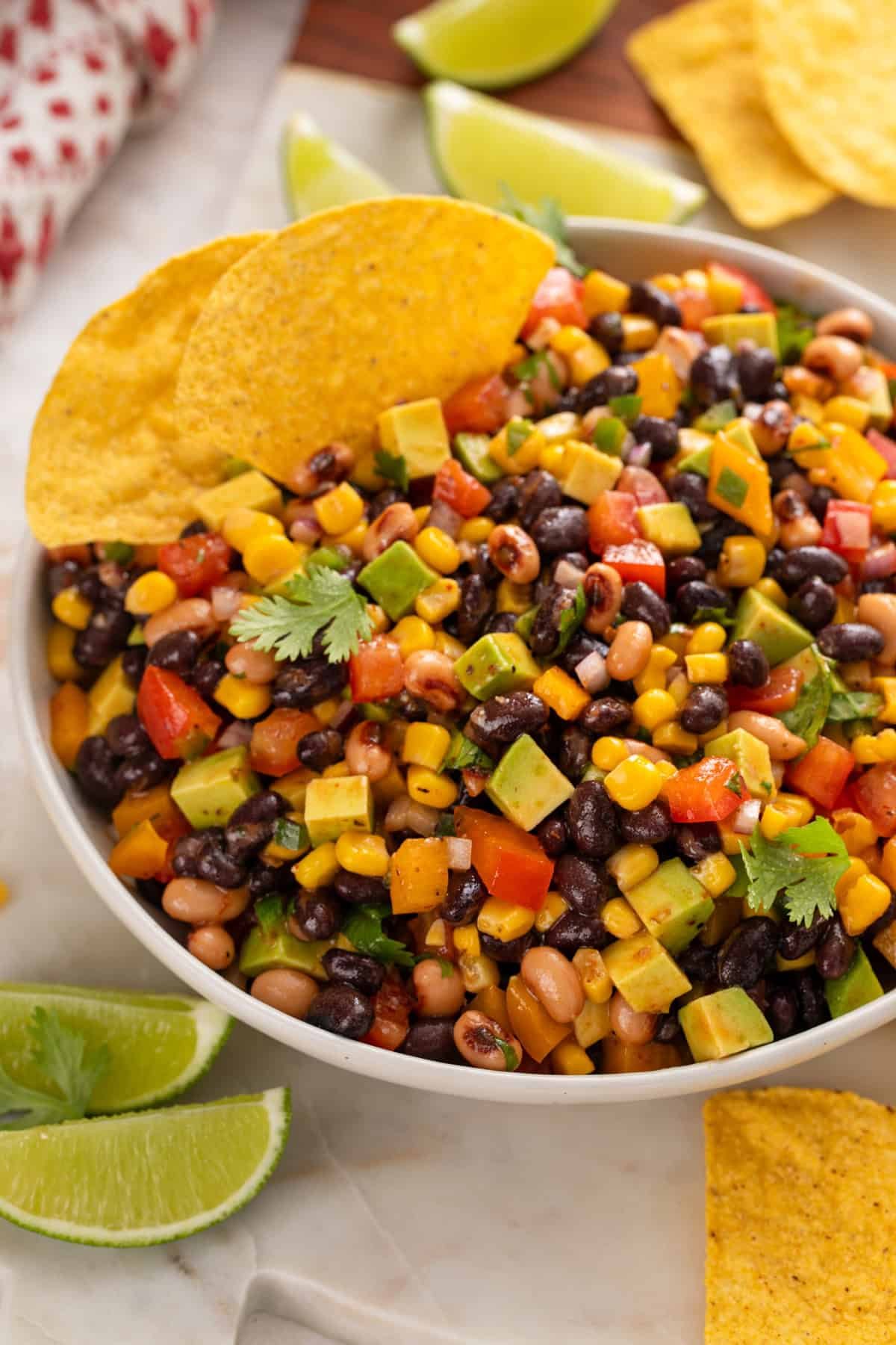 Cowboy caviar in a white serving bowl with two tortilla chips tucked into the edge of the dip.