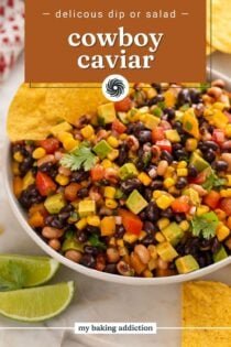 Cowboy caviar in a white serving bowl with two tortilla chips tucked into the edge of the dip. Text overlay includes recipe name.