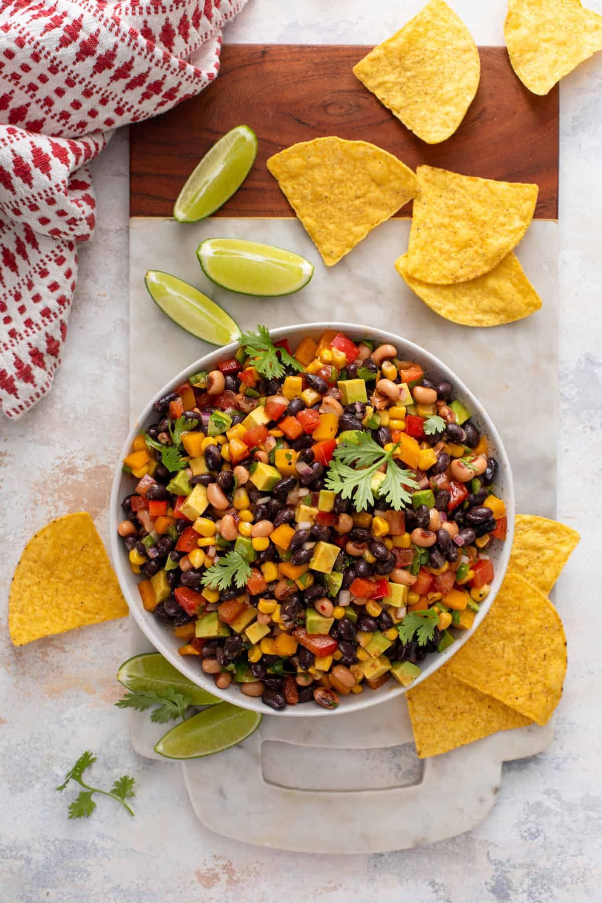 Overhead shot of a bowl of cowboy caviar surrounded by tortilla chips and lime wedges.