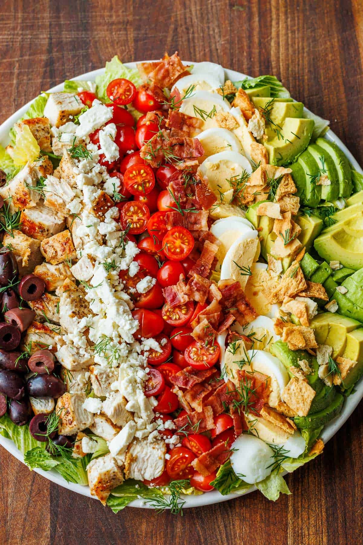 Greek Cobb Salad with ingredients in rows including olives, chicken, feta cheese, tomatoes, eggs, pita chips and avocado