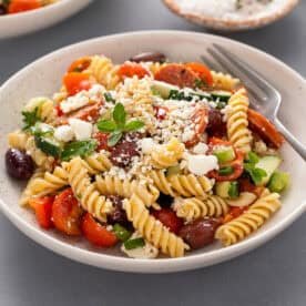 Greek pasta salad with a fork in a white bowl.